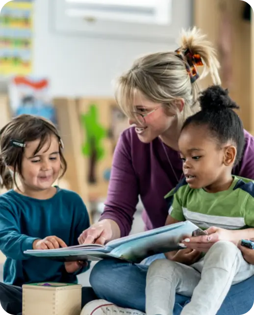 Teacher reading a book with two young students.