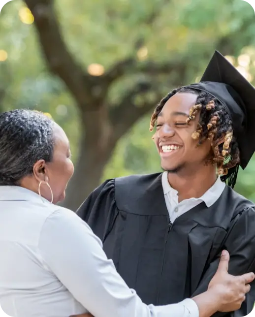Graduate smiling with a woman at an outdoor graduation.