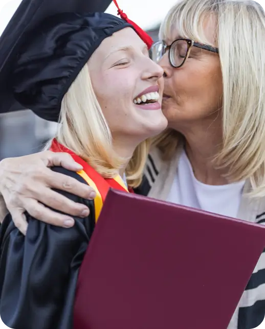Woman kissing a smiling graduate holding a diploma.