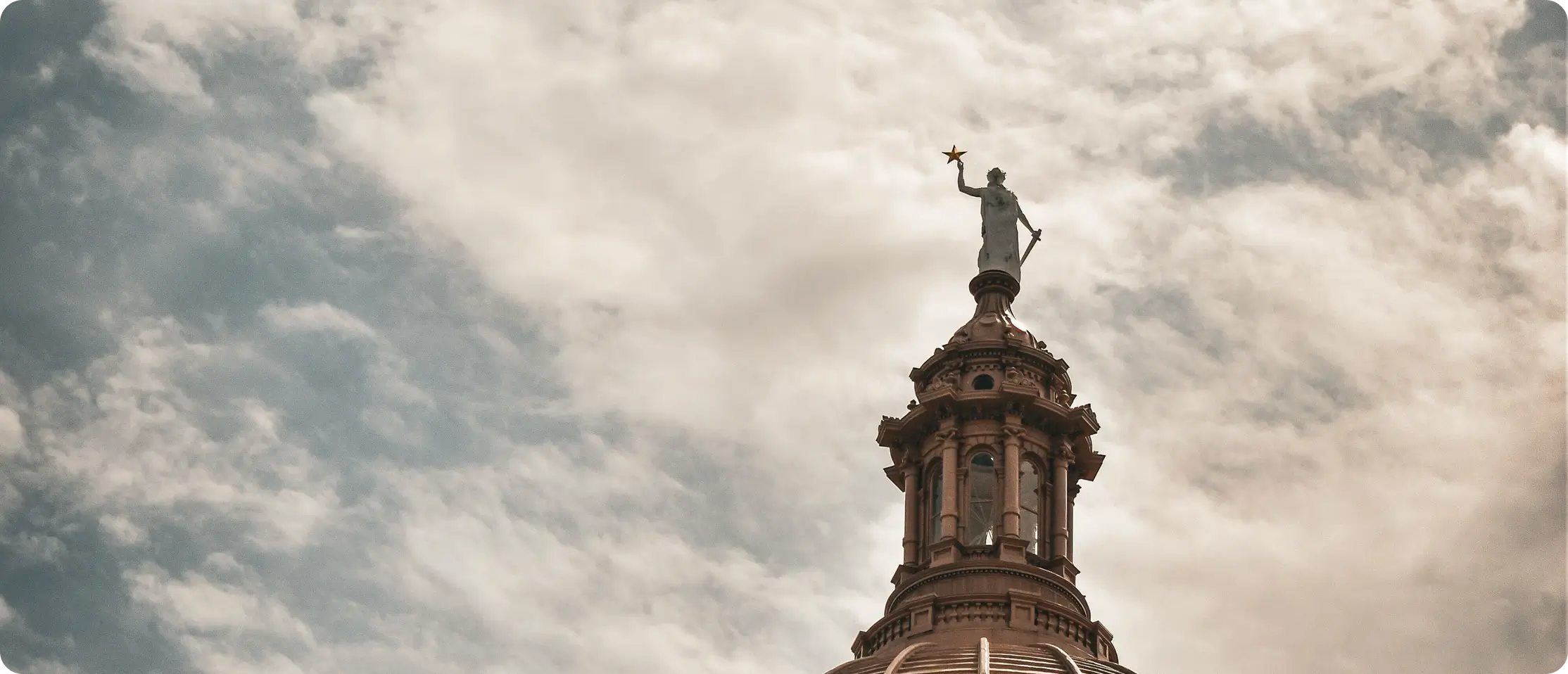 Goddess of Liberty statue atop the Texas State Capitol dome beneath a cloudy sky.